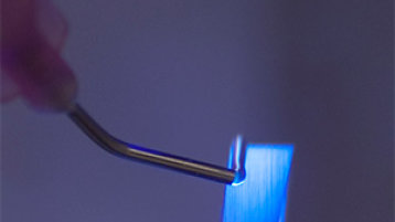 Eine Dosiernadel trägt einen Strang aus photoreaktivem Polymer auf den Rand des Brillenglases auf. 