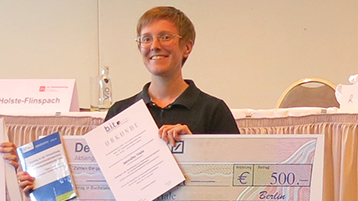 Jennifer Hale hält Urkunde und symbolischen Scheck in die Kamera (Bild: Prof. Dr. Achim Oßwald / TH Köln)