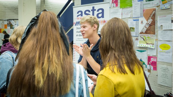 Am Stand des AStA erklärt ein junger Mann mehreren Zuhörerinnen etwas