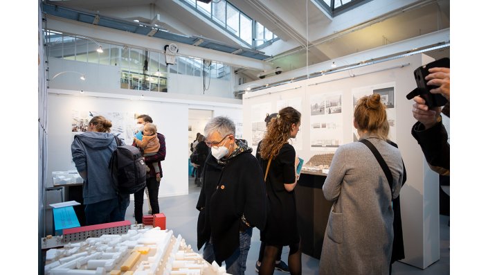 Besucher*innen der Ausstellung schauen sich die prämierten Abschlussarbeiten an.