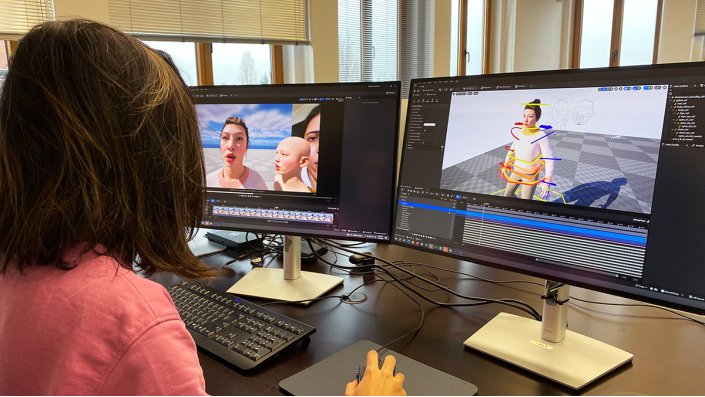 Eine Person sitzt vor zwei Monitoren, auf denen hyperrealistische Avatare zu sehen 