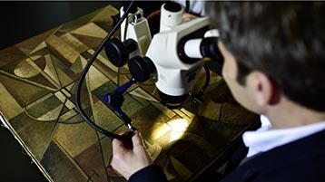 Prof. Dr. Gunnar Heydenreich untersucht mit einem Mikroskop ein Gemälde. (Bild: Costa Belibasakis / TH Köln)