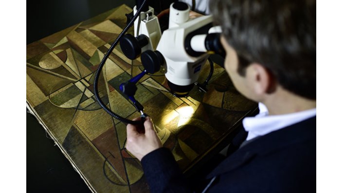 Prof. Dr. Gunnar Heydenreich untersucht mit einem Mikroskop ein Gemälde.
