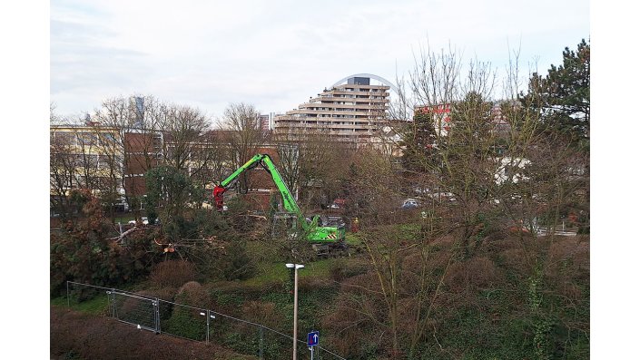 Blick auf die Baustelle, auf der ein grüner Bagger steht.