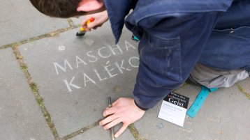 Person, die einen Stolperstein zum Gedenken der Opfer des Nationalsozialismus mit einem Pinsel bearbeitet (Bild: Markus Lokai / TH Köln)