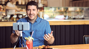 Infliuencer filmt sich mit dem Handy in einer Gastronomie (Bild: DanRentea/AdobeStock)