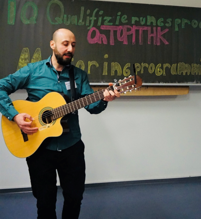 Der Teilnehmer Ayham Nabuti spielt im Stehen Gitarre. Er steht vor einer Tafel. 