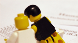 Zwei Playmobilfiguren knieen auf einem beschriebenen Blatt Zwei Playmobilfiguren knieen auf einem beschriebenen Blatt