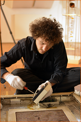 Maximilian Mämpel öffnet die teilweise defekte Steuerungselektronik eines lichtkinetischen Nagelobjektes von Günther Uecker