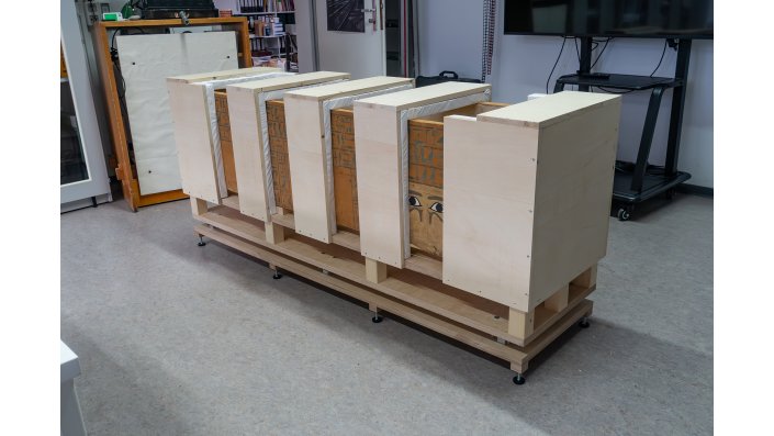 Das Bild zeigt den Sarg bei einem Probeaufbau auf dem Spezialsockel und mit den Brücken zur sicheren Befestigung des Sargs am Transport- und Ausstellungssockel.