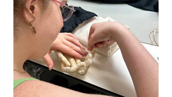 Nahaufnahme einer Studentin die eine Hand der textilen Figur "Desdemona" behandelt.