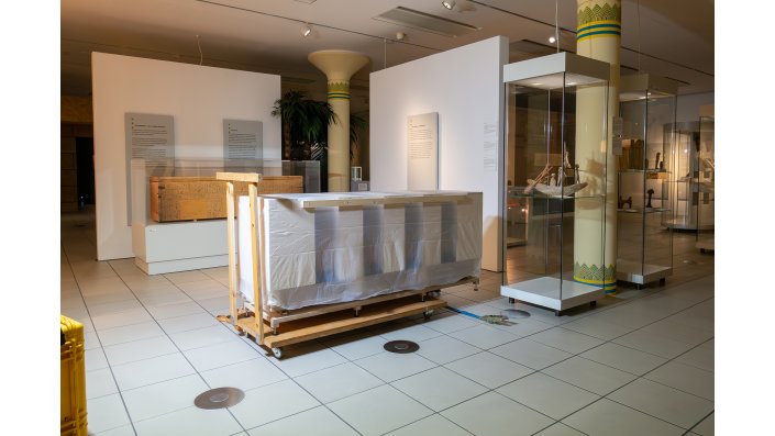 Hier steht der Sarg in seiner Transportverpackung in Ausstellungsraum der Ägyptischen Sammlung. Im Hintergrund ist eine "Attrappe" des Sarges in dem alten Showcase zu sehen.