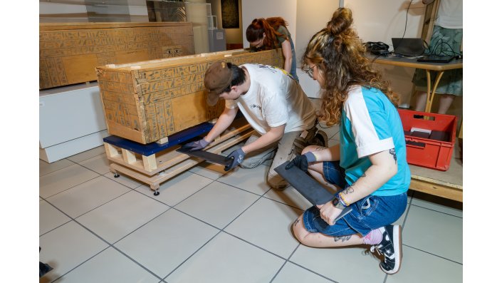 Anna-Lena Korsten und Jakob Becker legen die Gewichte in die dafür vorgesehenen Hohlräume des neuen Sockels. Durch die erhöhte Masse der Sarg-Sockel-Einheit und in Kombination mit den präzise abgestimmten Drahtseilfedern kann die Frequenz der Schwingungen auf die gewünschten Werte eingestellt werden.