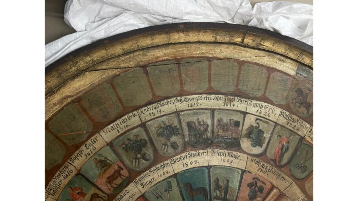 Einige Felder wurden für die noch folgenden Eintragungen der Zunftmitglieder in der zweiten Bemalungsebene bereits als Blamko-Felder angelegt. Durch die grünlich-graue Farbe der Platzhalter lassen sich Details der Bilddarstellungen der ersten Bemalungsebene erkennen.