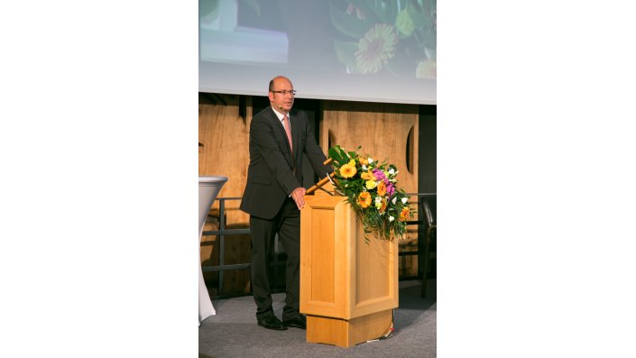 Prof. Stefan Materne begrüßt, am Rednerpult stehend, die Teilnehmer des Rückversicherungs-Symposiums