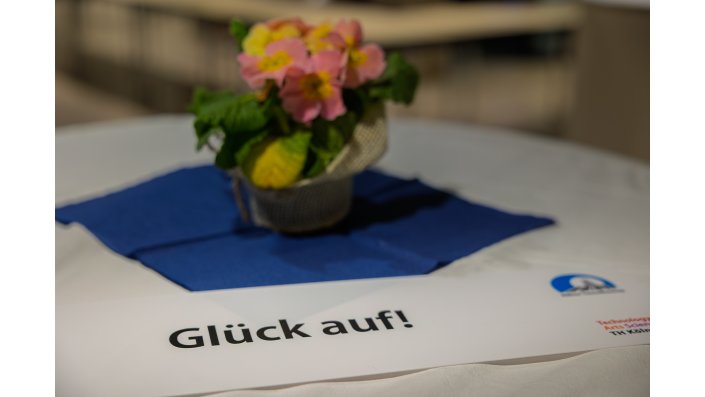Eine Blume auf einem Tisch. Davor eine Karte mit der Aufschrift "Glück auf!"