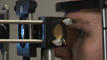 Ansicht von der Seite auf Person sistzend in einem OCT Messaufbau zur vermessung des Auges (Bild: PAM3 2021 / TH Köln)