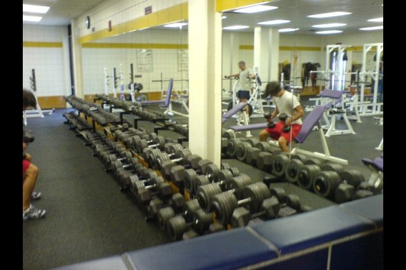 Fitnesscenter: im Vordergrund viele Gewichte, im Hintergrund Geräte