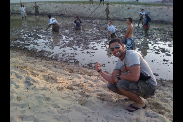 Ein junger Mann zeigt lachend auf weitere jungen Leute, die knietief durch nassen Sand waten