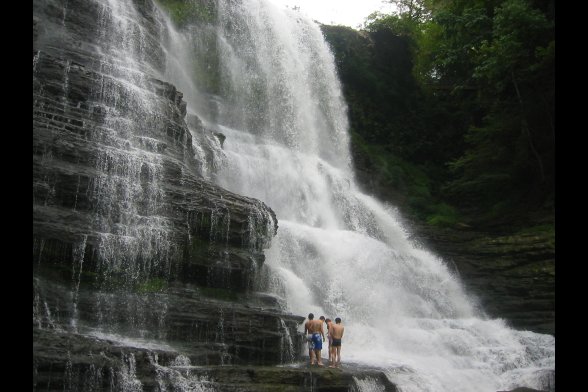 Vier Männer in Badehosen stehen neben einem etwa 20m hohen Wasserfall