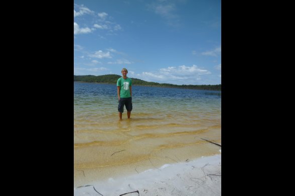 Junger Mann steht mit dem Füßen im Wasser am Strand