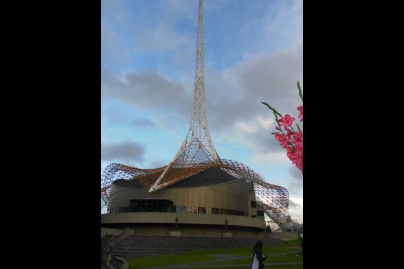 Futuristisches gebäude mit einem Stahlnetzdach das in einen Spitzen Turm mündet