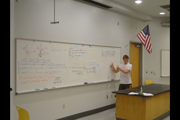 Ein junger Mann steht an einem großen Whiteboard in einem Seminarraum, neben der Tür hängt eine Flagge der USA