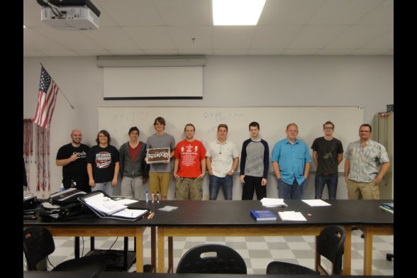 Zehn Männer stehen an einer Wand in einem Seminarraum