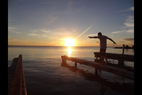 Junger Mann balanciert im Sonnenuntergang auf einem Steg, der ins Wasser hinein reicht