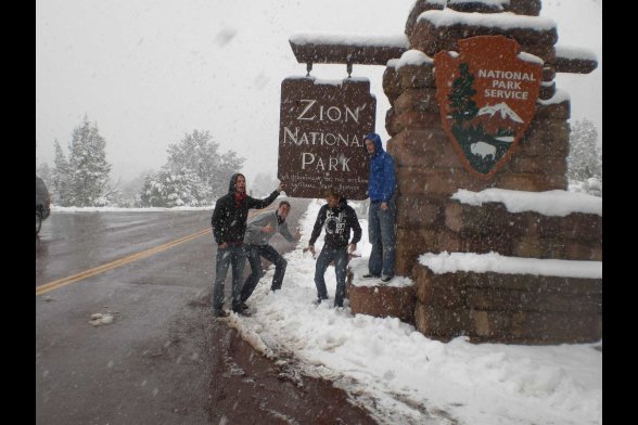 Drei junge Männer vor dem verschneiten Eingangsschild des Zion National Parks
