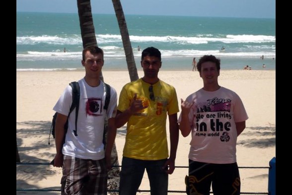 drei junge Männer vor einem Palmenstamm am Strand