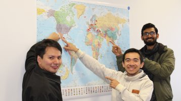 Drei junge Männer zeigen auf ihr Herkunftsland auf einer Landkarte. Drei junge Männer zeigen auf ihr Herkunftsland auf einer Landkarte.