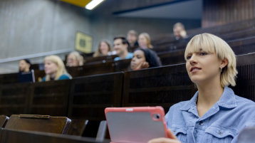 Nahaufnahme einer weiblich gelesenen Studierenden in einem Vorlesungsaal, im Hintergrund unscharf weitere Studierende (Bild: Hanna Witte/TH Köln)