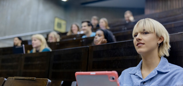 Nahaufnahme einer weiblich gelesenen Studierenden in einem Vorlesungsaal, im Hintergrund unscharf weitere Studierende (Bild:Hanna Witte/TH Köln)