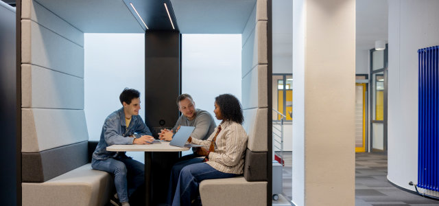 Drei Studierende arbeiten in einer modernen Lernbox am Campus Deutz zusammen. Eine Person nutzt einen Laptop, die anderen sprechen miteinander an einem Tisch. (Bild:Hanna Witte/TH Köln)