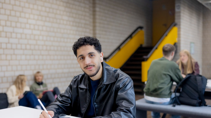Ein männlich gelesener Studierender arbeitet mit einem iPad im Gebäude am Campus Deutz. Im Hintergrund arbeiten weitere Studierende
