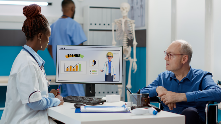 Ärztin und Patient schauen auf Monitor, der die HINT-App mit Avatar anzeigt.