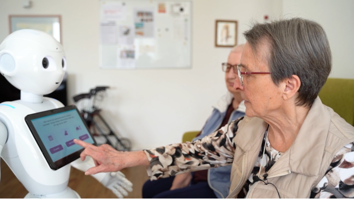 Eine Dame tippt auf das Tablet von Pepper dem Roboter