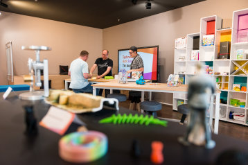 Lehrgespräch unter 3 Personen, im Vordergrund sind unscharf verschiedene 3D-Drucke zu erkennen Lehrgespräch unter 3 Personen, im Vordergrund sind unscharf verschiedene 3D-Drucke zu erkennen