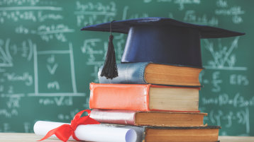  Stack books graduate hat and diploma in front of green chalkboard (Bild: 196875700_sebra_AdobeStock_)