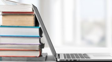 Bücherstapel liegt auf einem Tisch. Daneben steht ein aufgeklappter Laptop (Bild: IStock / artisteer)