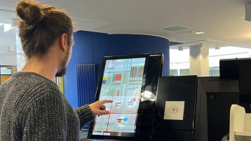 Eine Person steht vor einem Selbstverbucher und wählt auf dem Touchscreen die gewünschte Funktion aus (Bild: TH Köln/ Alina Beier)