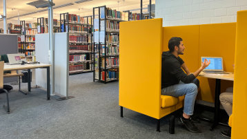 Blick in den Lesesaal mit Bücherregalen, Lernplätzen und einer gelben Sitzecke mit Personen (Bild: TH Köln/ Alina Beier)