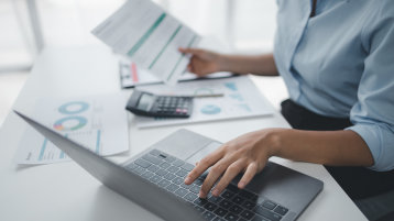 Eine Person arbeitet am Schreibtisch mit Laptop, Unterlagen und Taschenrechner (Bild: Adobe Stock 637777215 Kamiphotos) Eine Person arbeitet am Schreibtisch mit Laptop, Unterlagen und Taschenrechner (Bild: Adobe Stock 637777215 Kamiphotos)