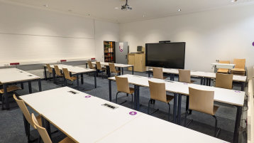 Blick in den weitläufigen Schulungsraum. Es gibt mehrere Tischreihen mit Stühlen. Im vorderen Bereich steht ein mobiles SmartBoard an der Wand. (Bild: TH Köln/ Anja Kremser)
