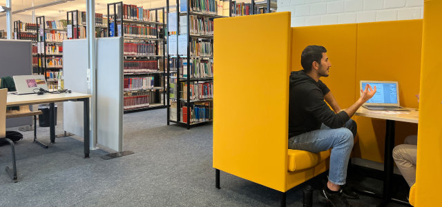 Blick in den Lesesaal mit Bücherregalen, Lernplätzen und einer gelben Sitzecke mit Personen (Bild:TH Köln/ Alina Beier)