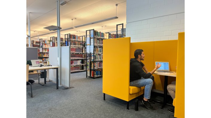 Blick in den Lesesaal mit Bücherregalen, Lernplätzen und einer gelben Sitzecke mit Personen