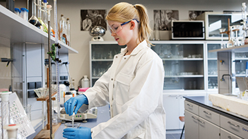 Eine junge Frau steht in einem weißen Kittel in einem Labor (Bild: TH Köln)