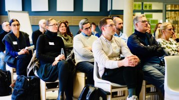 Die Teilnehmenden sitzen auf Stühlen und blicken zur Leinwand, die man im Bild nicht sieht. (Bild: ZLE TH Köln)