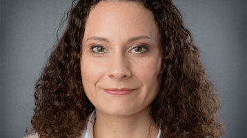 Frau Castro-Lesching steht vor einem dunkelgrauen Hintergrund. Sie hat dunkelbraune, gelockte Haare und trägt einen beigen Blazer sowie eine weiße Bluse. (Bild: Castro-Lesching)